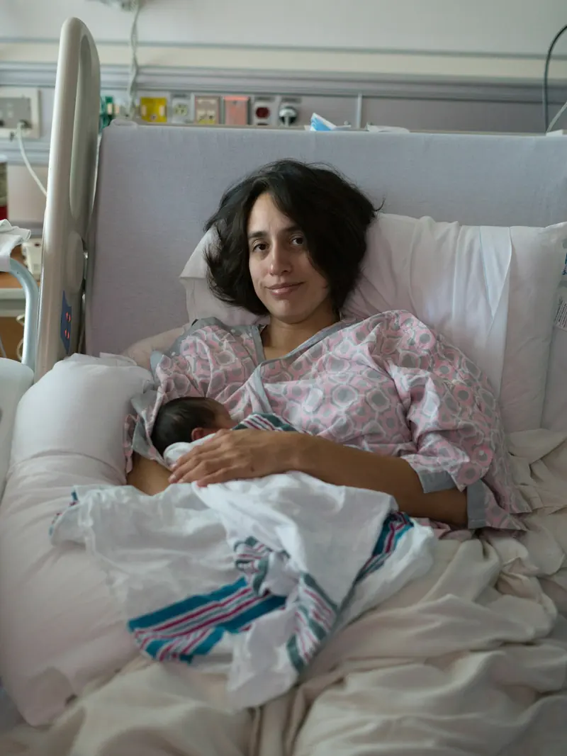 Eine Mutter sitzt im Spitalbett und hält ihr Neugeborenes
